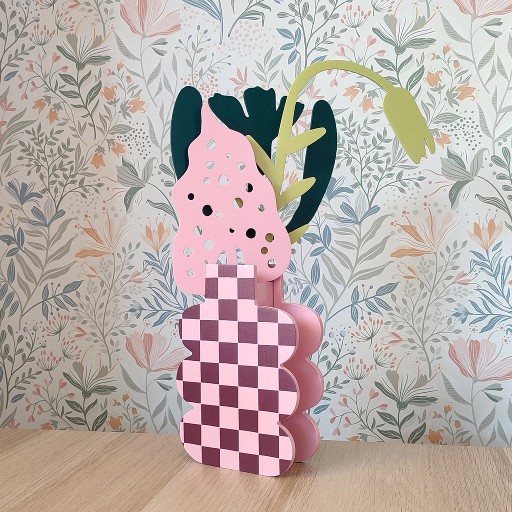Mazzo di fiori in legno, su vaso a scacchi rosa, su sfondo floreale e piano in legno chiaro, BECCA