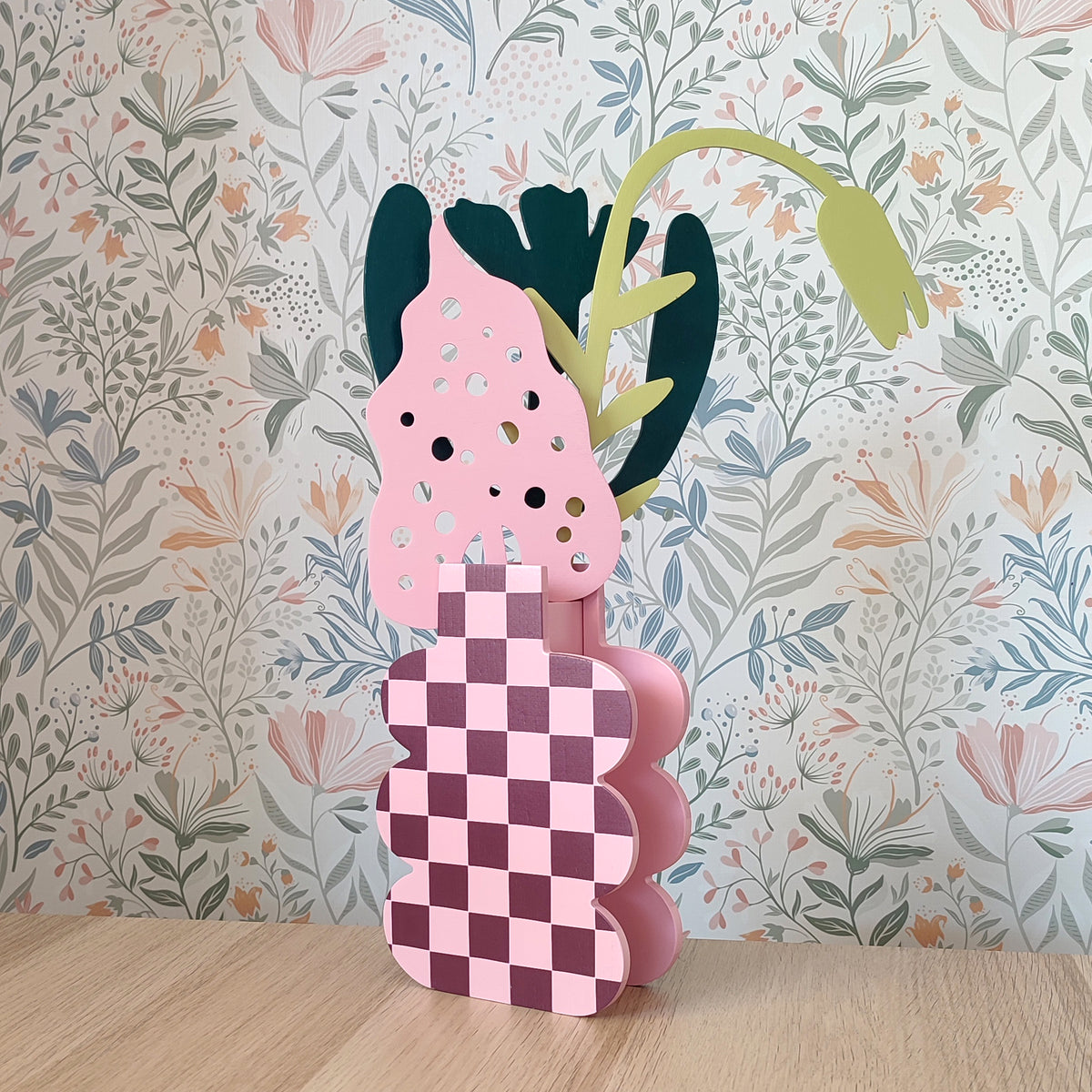 Mazzo di fiori in legno, su vaso a scacchi rosa, su sfondo floreale e piano in legno chiaro, BECCA