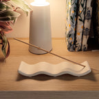 Porta incenso Wave bianco, visto dall'alto, su mobile di legno, con lampada e libri e pianta, BECCA
