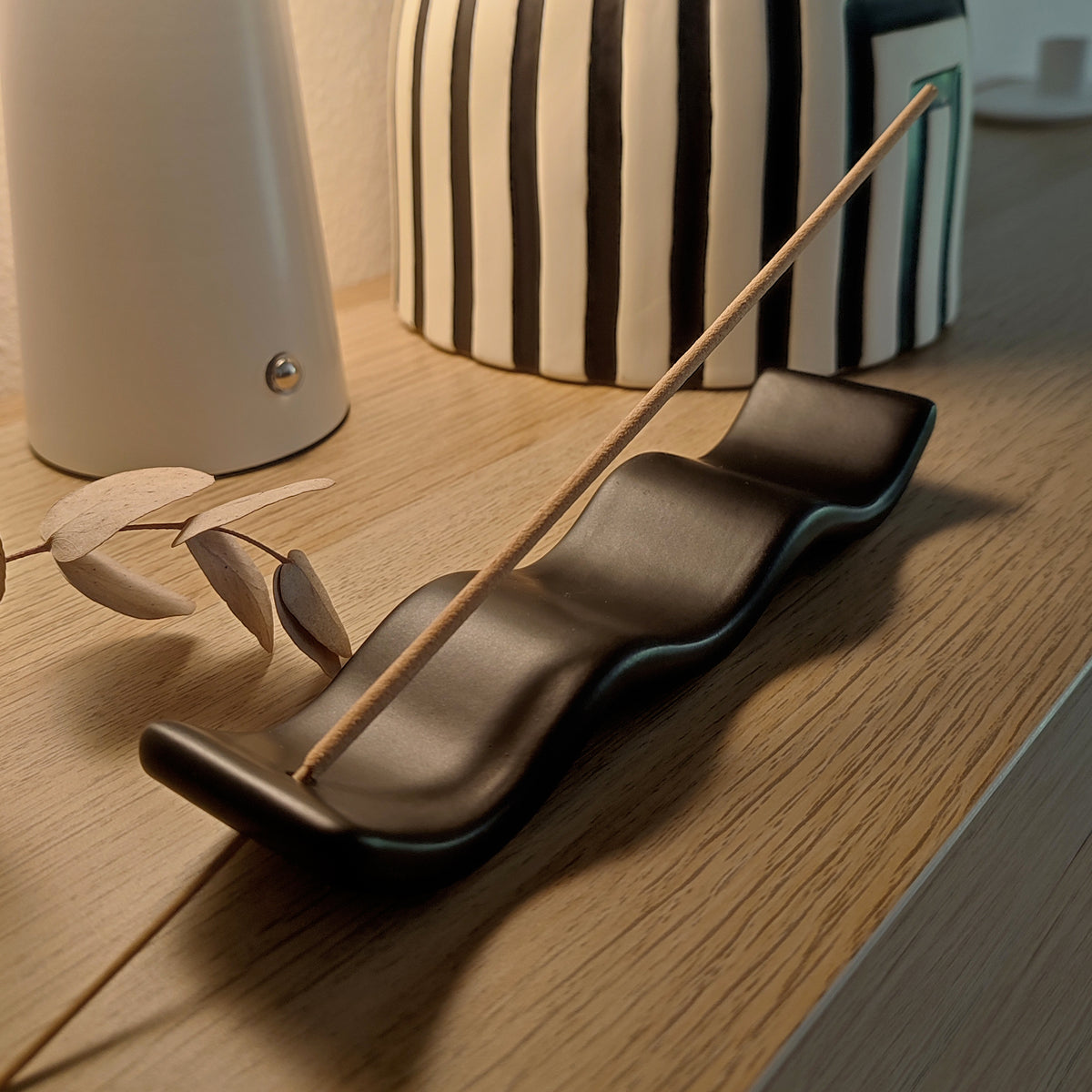 Porta incenso Wave, nero, con incenso, su ripiano in legno con altri elementi decorativi, becca