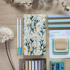 Quaderno Dery, copertina ricamo margherite bianche, su scrivania con post-it matite e puzzle, BECCA