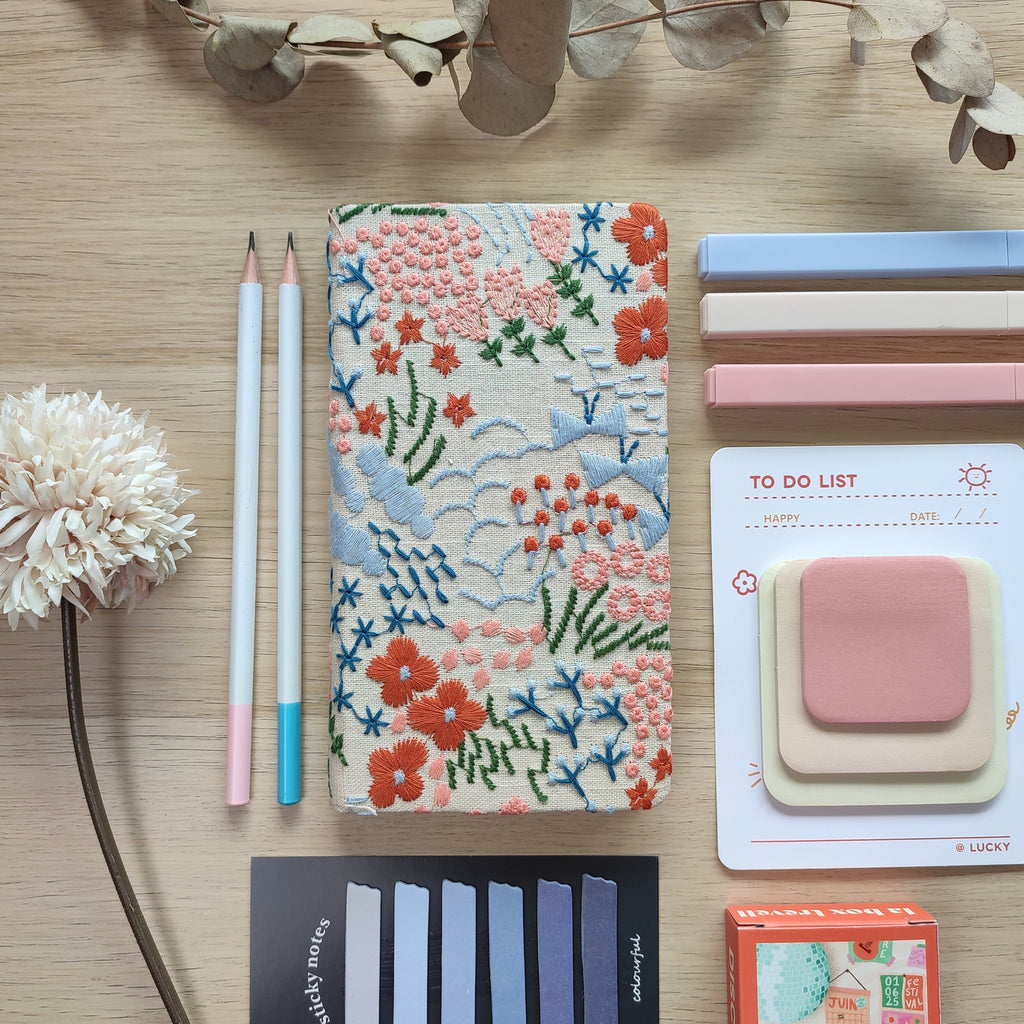 Quaderno Dery, copertina rigida con fiori ricamati, su scrivania in legno con matite post-it puzzle fiore, BECCA