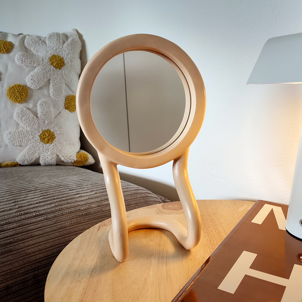 Specchio RORRI beige, base ondulata, specchio tondo, ambientato in un living, su tavolino da caffè