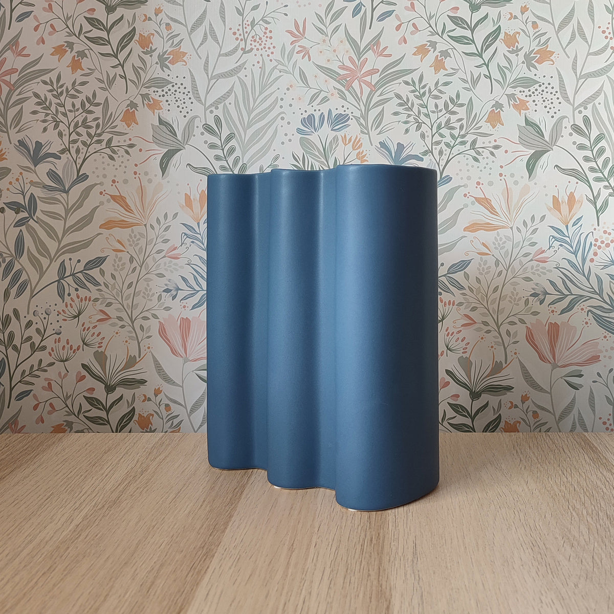 Vaso Onda, blu, in ceramica, vista laterale, su ripiano in legno, sfondo floreale, BECCA