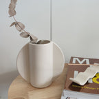 Dettaglio dall'alto del vaso TOO POT bianco con apertura circolare e manici laterali, su tavolino di legno e fiori secchi, becca