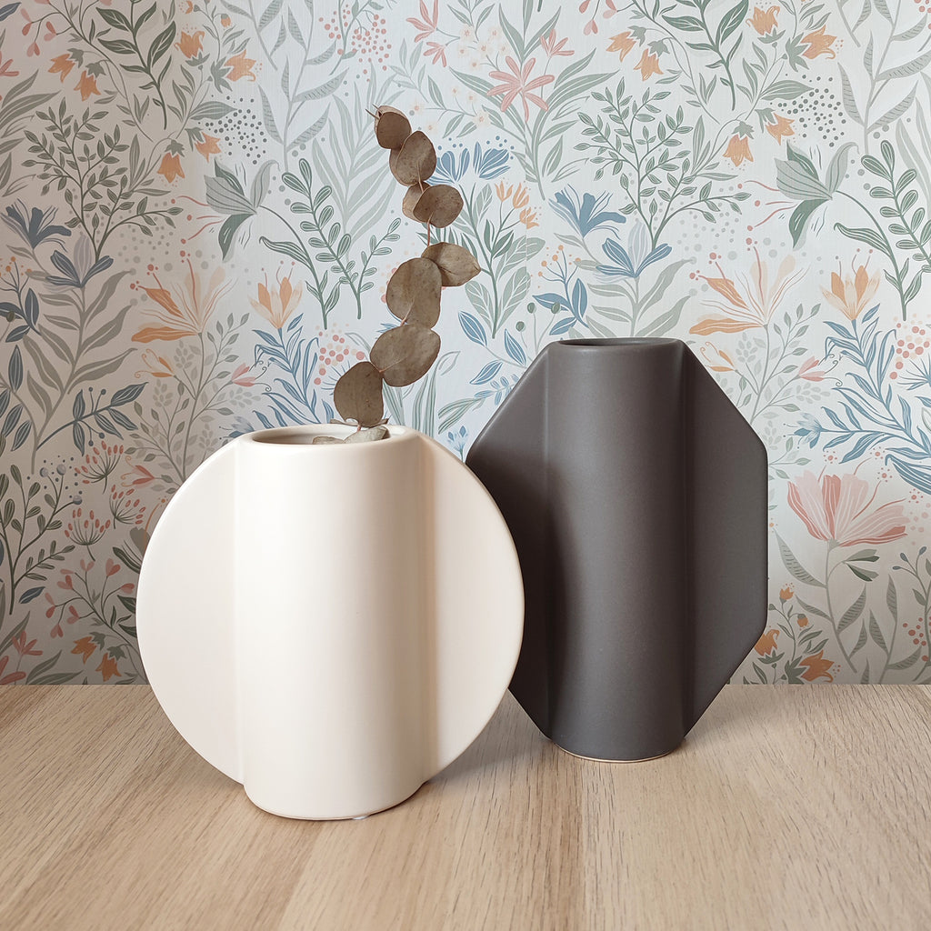 Vaso TOO POT grigio accanto al vaso TOO POT bianco su piano in legno con sfondo floreale, BECCA