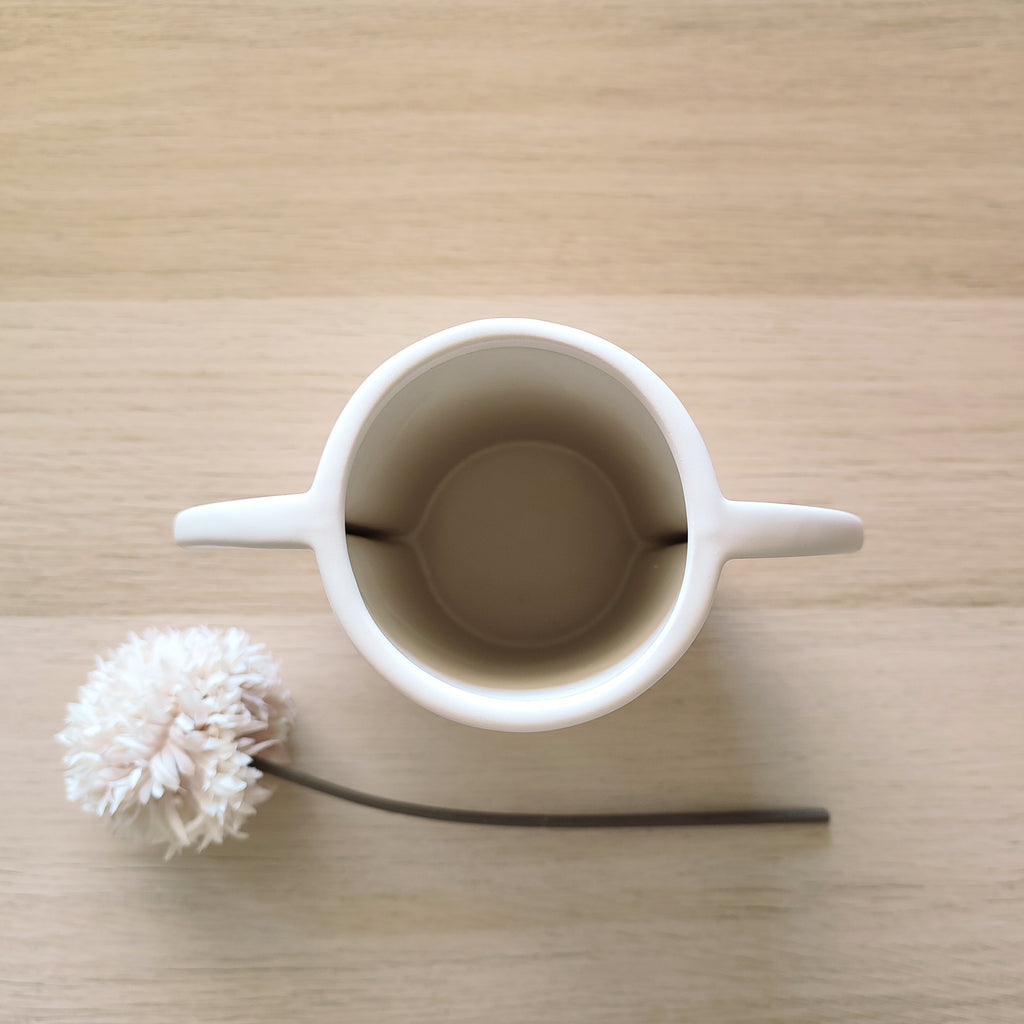Vista dall'alto del vaso TOO POT bianco con apertura e fiore secco bianco sul piano, BECCA